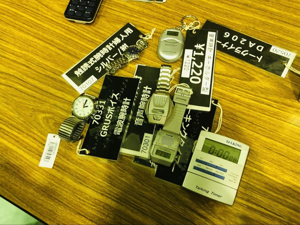 机の上に音声時計などの便利グッズがたくさん並んでいる画像
