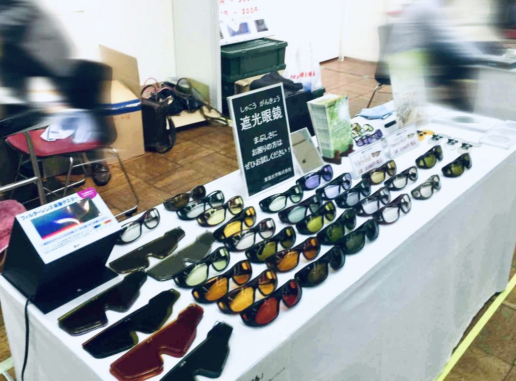 展示会で机の上にカラフルな遮光眼鏡やパンフレットが並んでいる画像