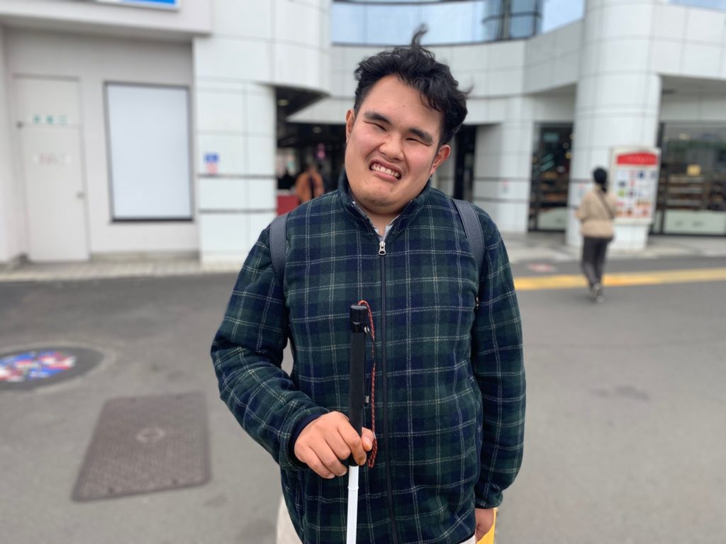 駅の前で立つ笑顔のはじさん