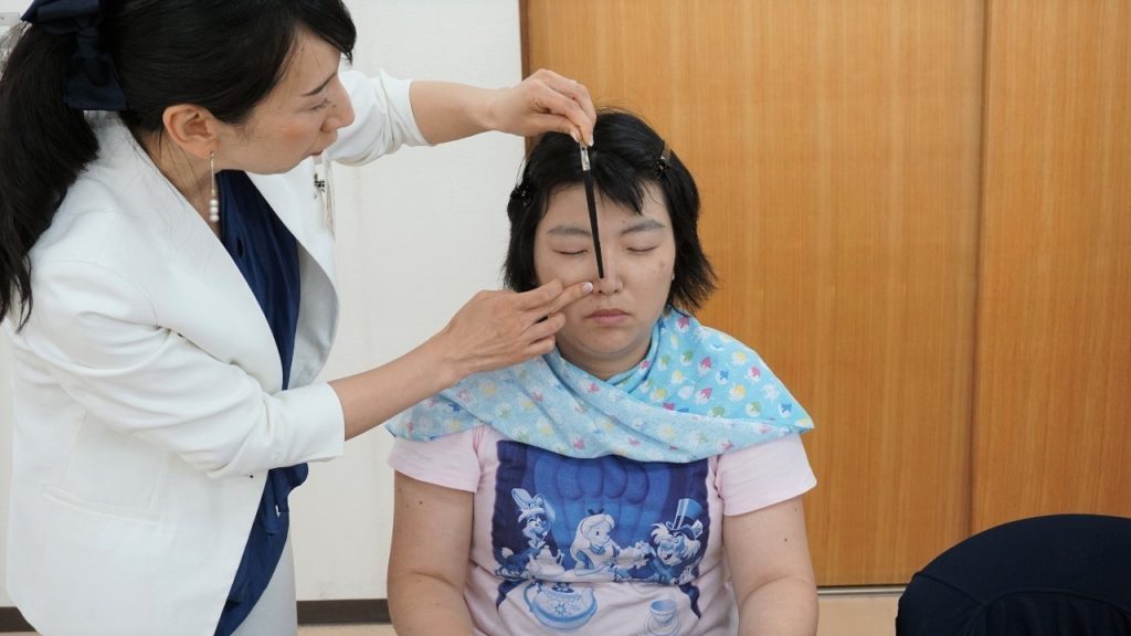 中川さんがブラシの柄を使って参加者の眉毛のバランスを確認している画像。