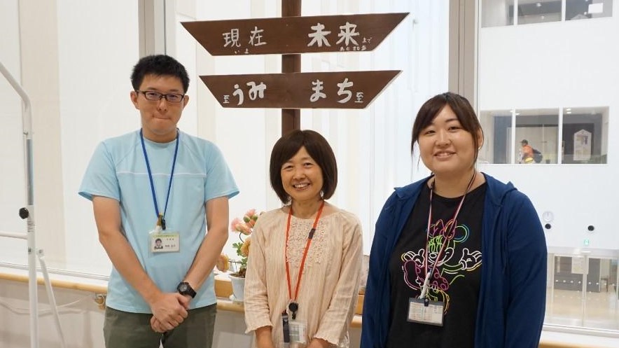 エレベータ前で訓練士三人が笑顔で並んでいる画像