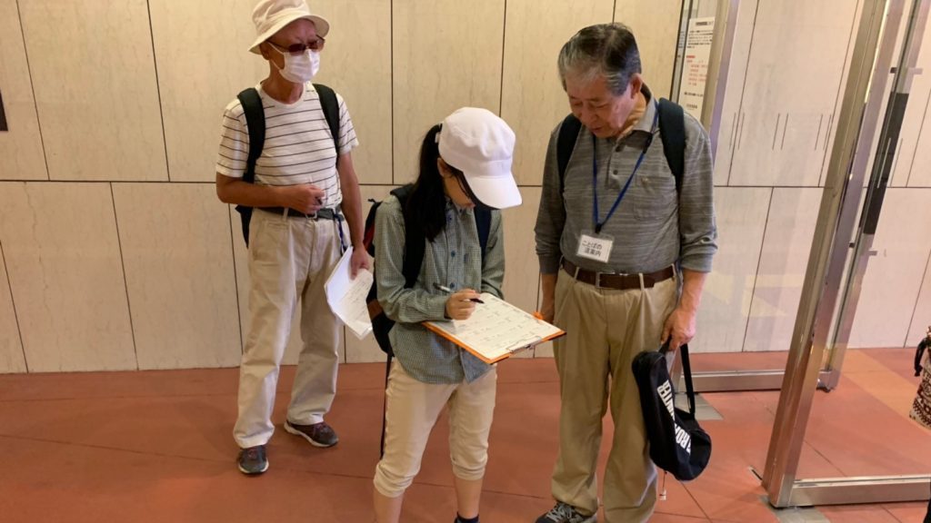 駅構内で、ボランティアが必要な情報をメモしている画像