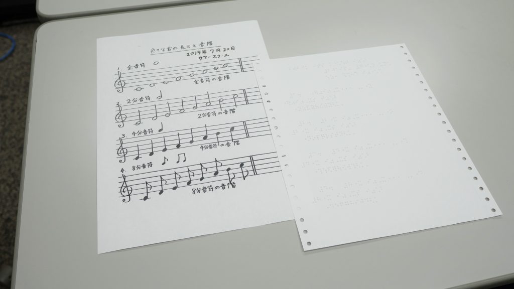 机の上に点字の楽譜と墨字の楽譜が置かれている画像。