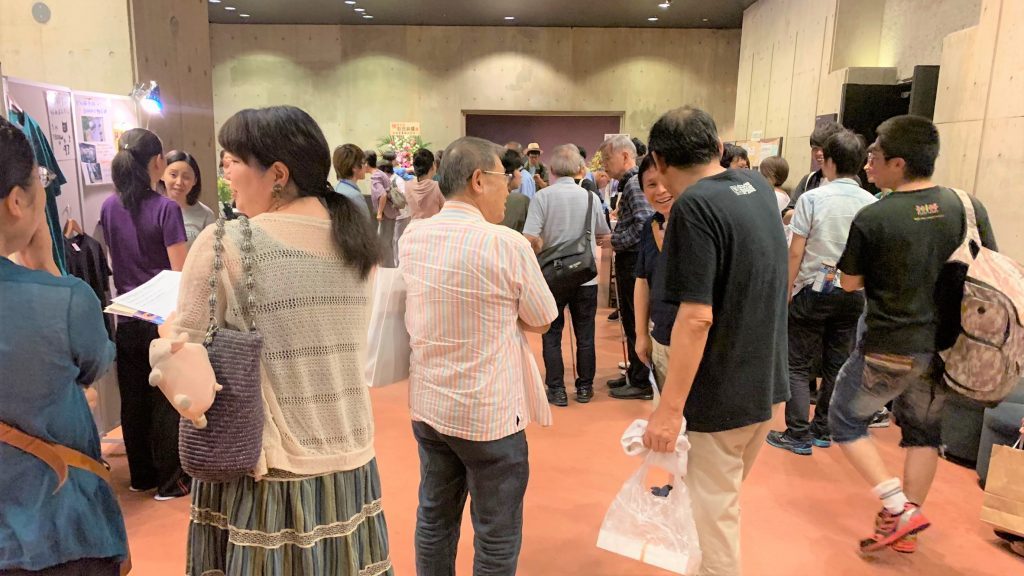 演劇終了後、ロビーで劇団員と観客が話をしている画像。
