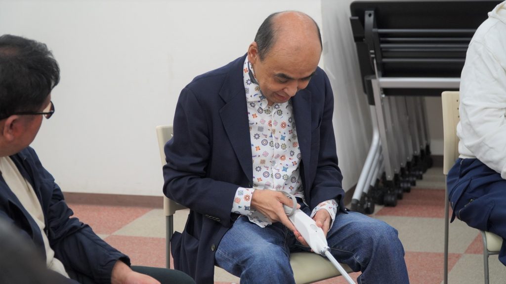 スマートケーンを手に、操作方法を説明する参加者の画像。
