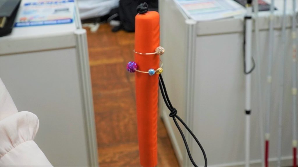白杖のグリップ部分にオシャレな石がついた指輪のような輪っかがついている画像。