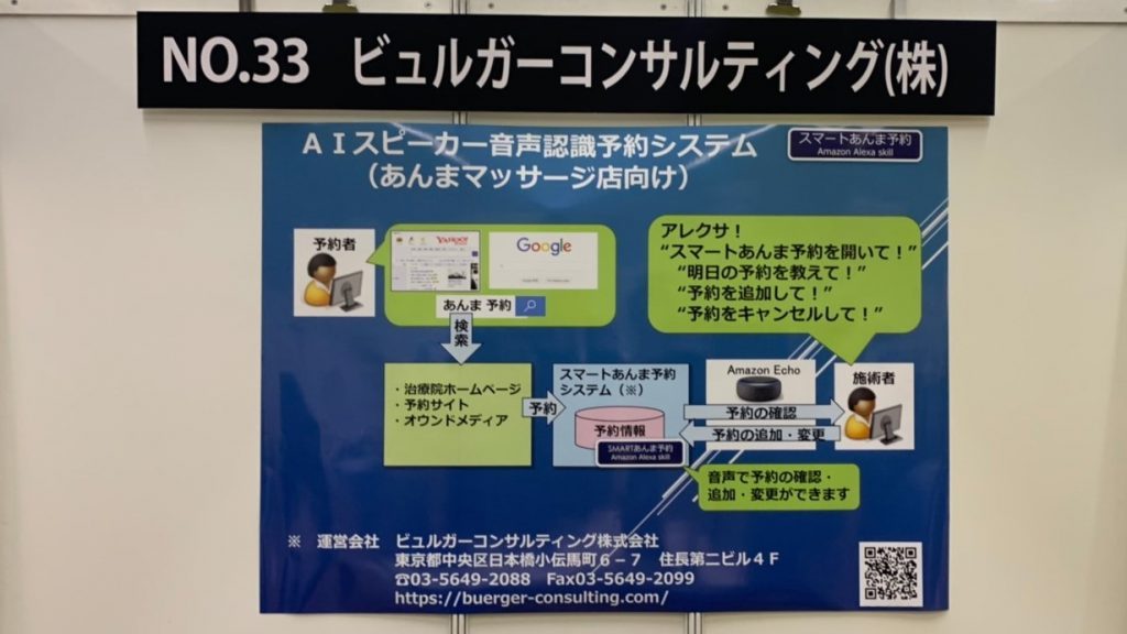 ブースの看板の下にシステムの概要を説明した紙が貼られている画像。