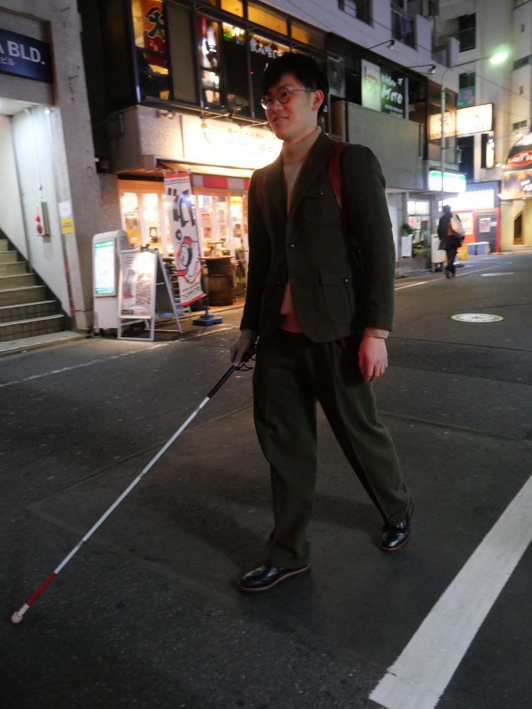 夜、人通りの少ない道を白杖を使って歩く宮食行次さん