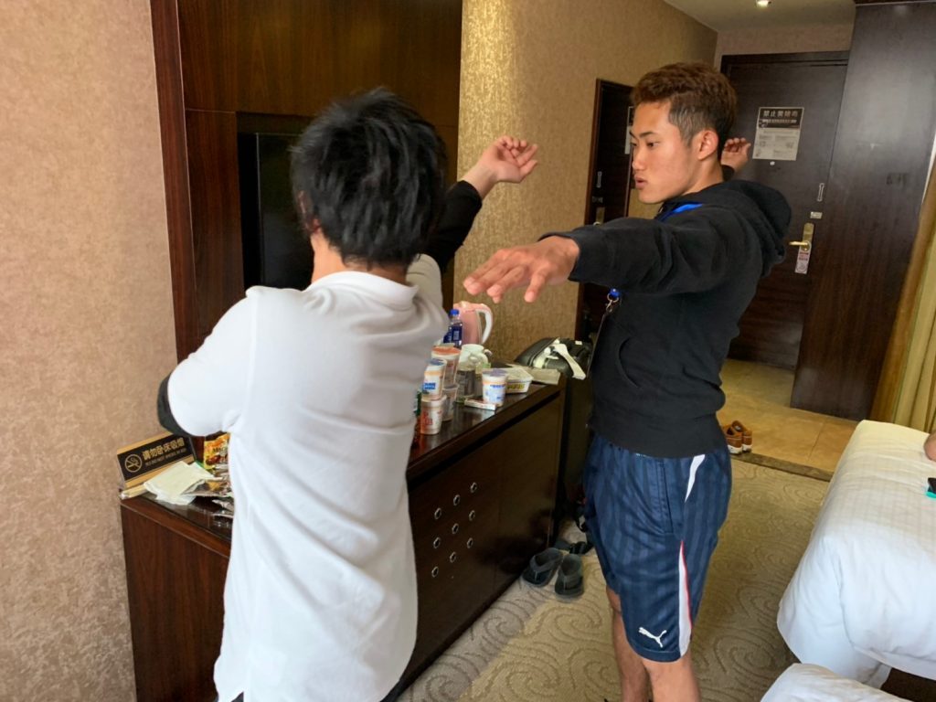 北京のホテルの部屋で、若生くんが田中さんのコーチからやり投げのフォームを教えてもらっている画像