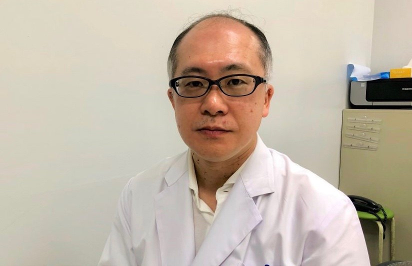 白衣を着た久米川先生の上半身を正面から撮影した画像