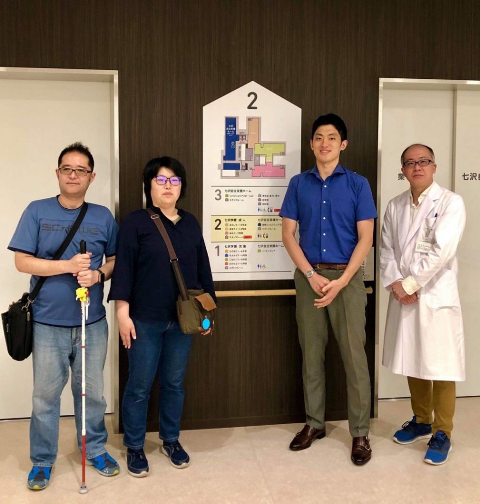 エレベーターの前で、久米川先生とSpotliteの渡辺、下田、高橋が記念撮影している画像。
