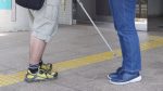 点字ブロックの上を歩く視覚障害者に声をかけている晴眼者を足元のみ撮影した画像