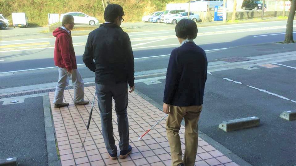 眼科の駐車場で、内野さんが患者に白杖の使い方を伝えている画像。