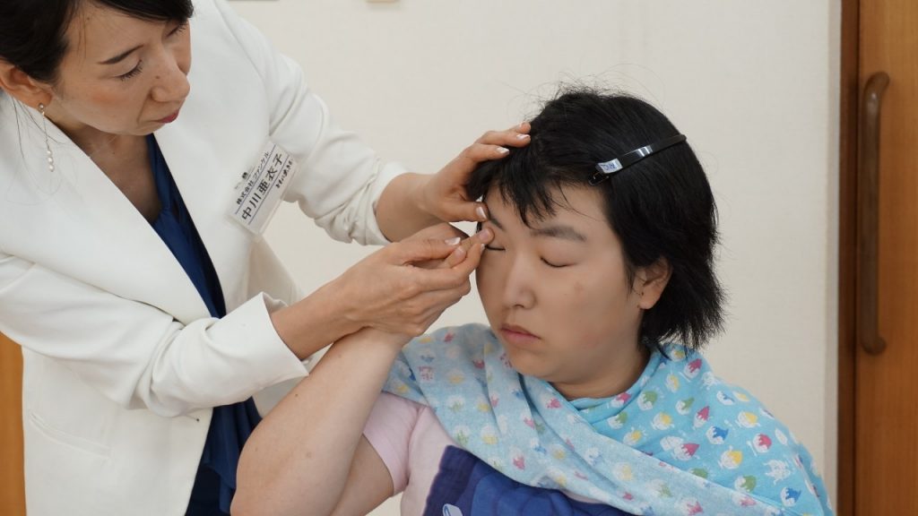 中川さんが参加者の薬指を持って、眉毛の上にチークを塗る画像。
