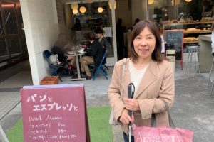 カフェの看板の横で丸山さんが笑顔で立っている画像。