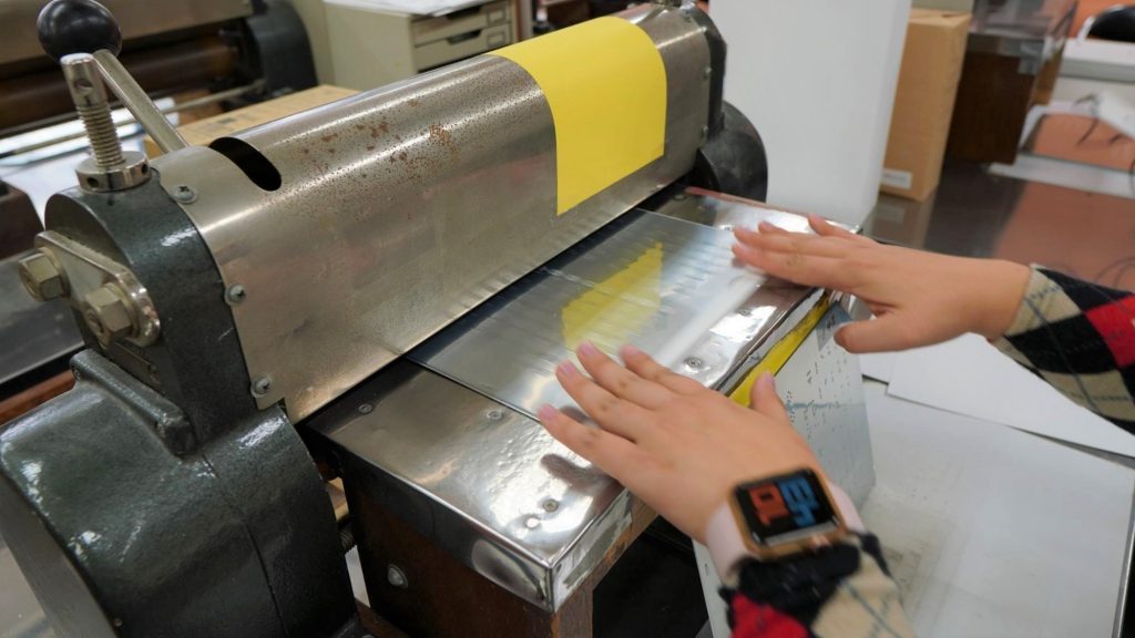 亜鉛板印刷を行う機械に亜鉛板を通している画像。