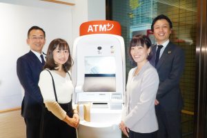 セブン銀行のATMの脇にスタッフ4名が笑顔で立っている画像。