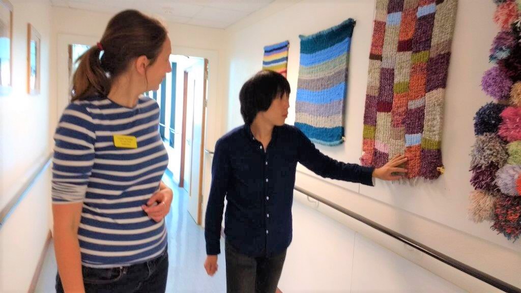 イギリスの施設で廊下の壁にかけられた織物を触る北原さんの画像。