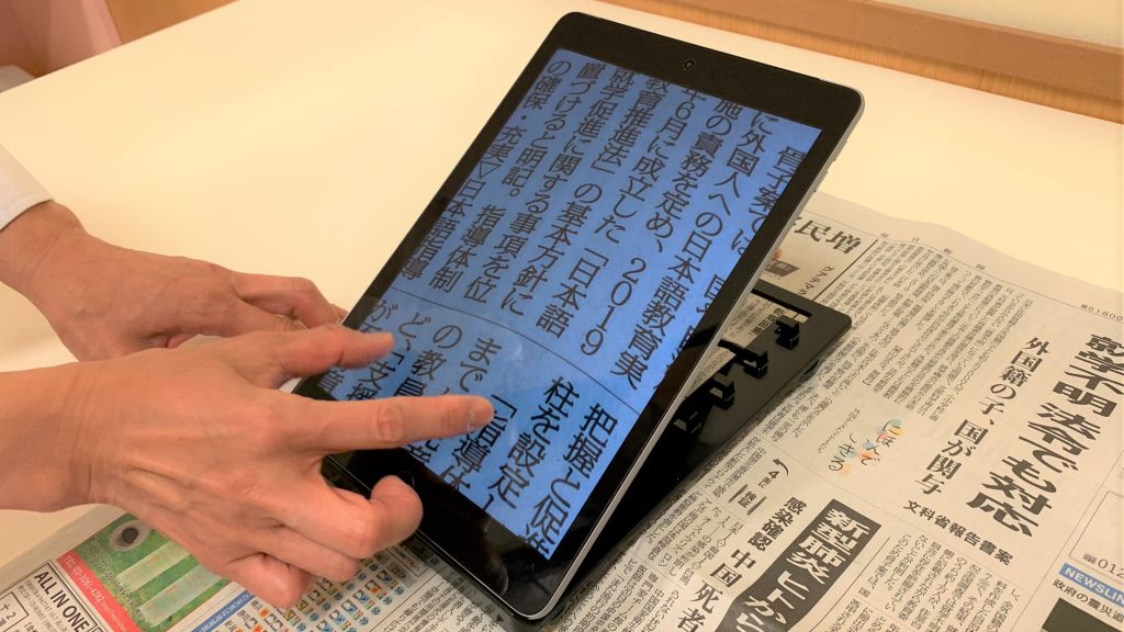 専用の台にiPadを乗せて新聞を拡大して読んでいる画像。