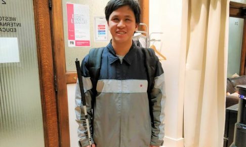 クレメントさんが白杖を持って笑顔で立っている画像。
