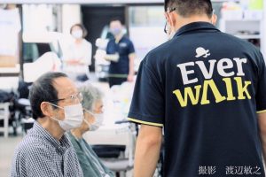 エバーウォークの職員が利用者と話をしている画像。職員の背中にエバーウォークのロゴが入っている。