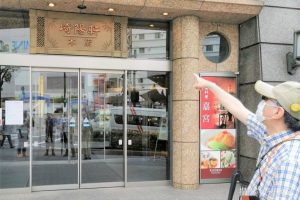 鈴木さんが崎陽軒のお店の前で、入口を指さしている画像。