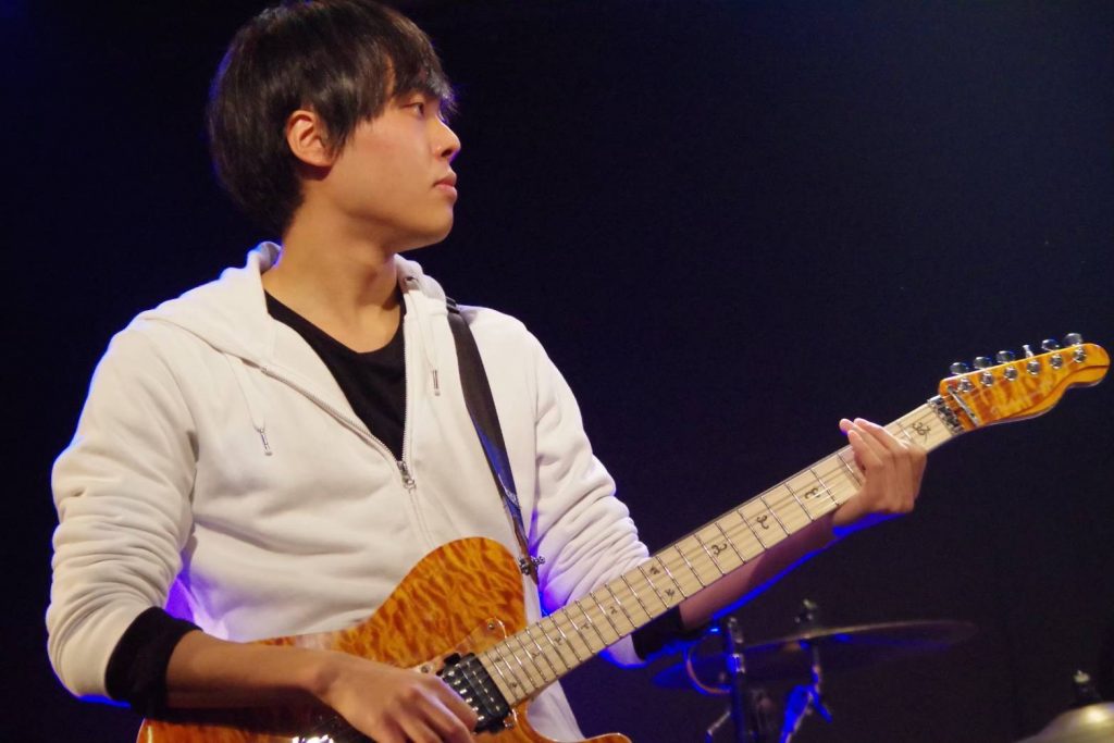 ライブでギターを弾いている三輪さんの横顔の画像。