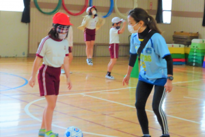 アイマスクをしてブラインドサッカーのボールをける子どもと横で見守るチームスタッフの画像。