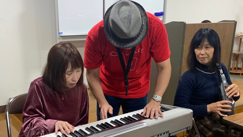 佐野さんが視覚障害者にエレクトーンの弾き方を教えている画像。