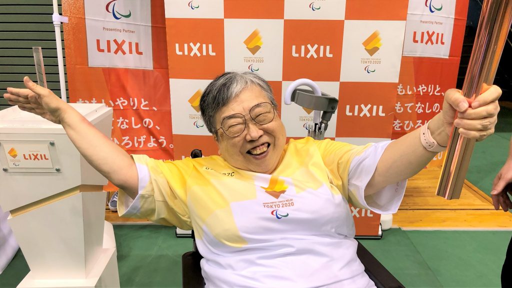 聖火リレー会場でトーチを持って満面の笑みを浮かべる吉野さんの画像。