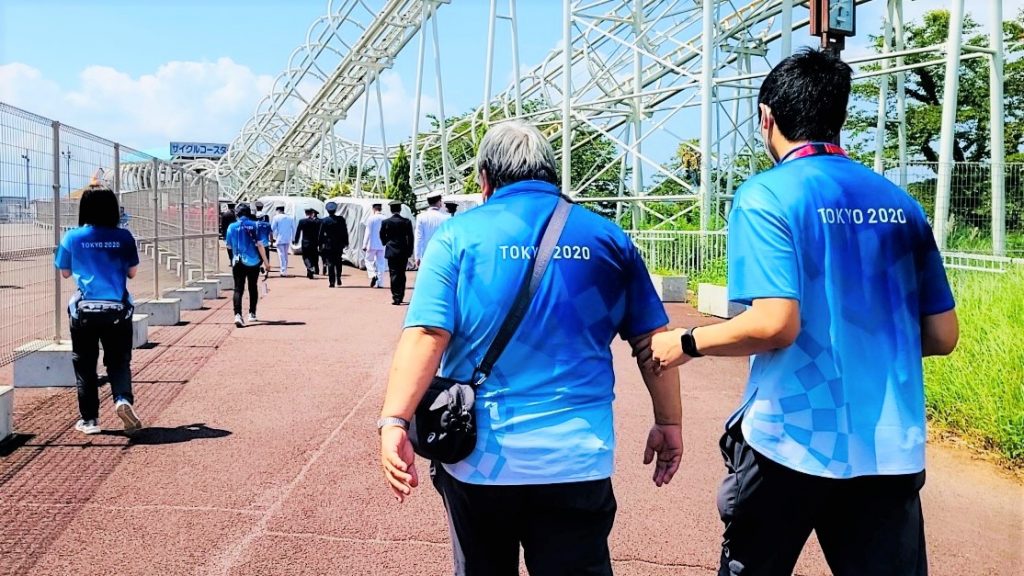 村松さんが誘導者と一緒に、競技場の脇を歩いている後ろ姿の画像。