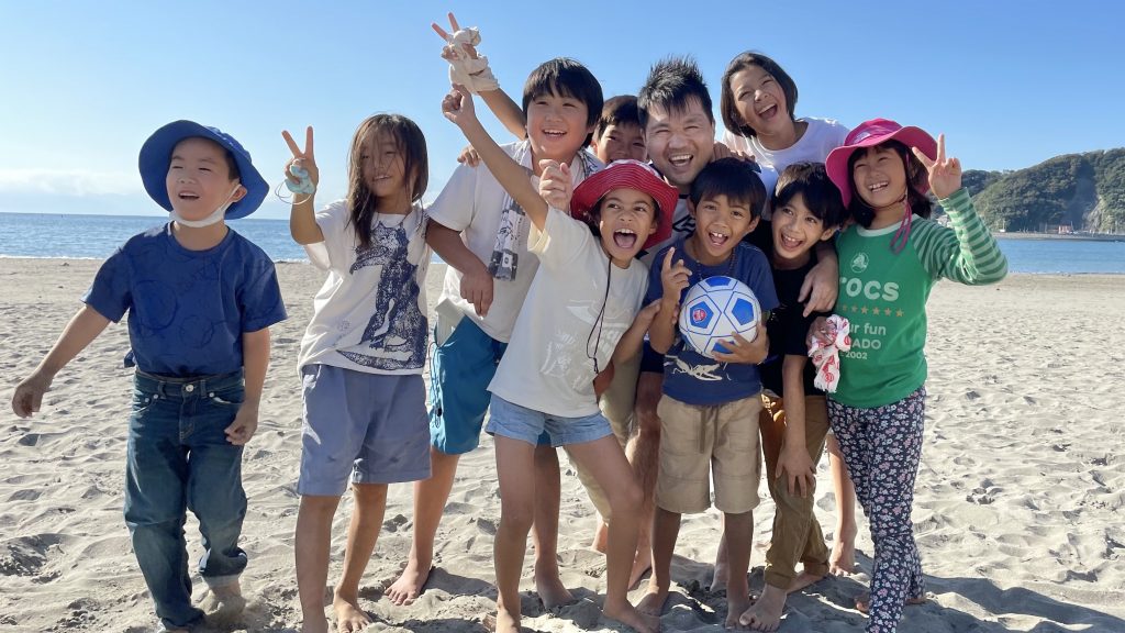 落合さんが砂浜で子供たちと一緒に笑顔で記念撮影している画像。