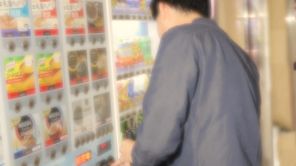 視覚障害者が自動販売機に顔を近づけてジュースを買おうとしているイメージ画像。