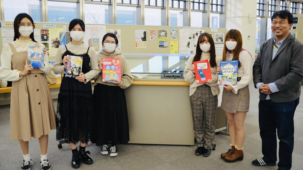 サークルの学生５人と元木さんが鶴見大学図書館の企画展で記念撮影している画像
