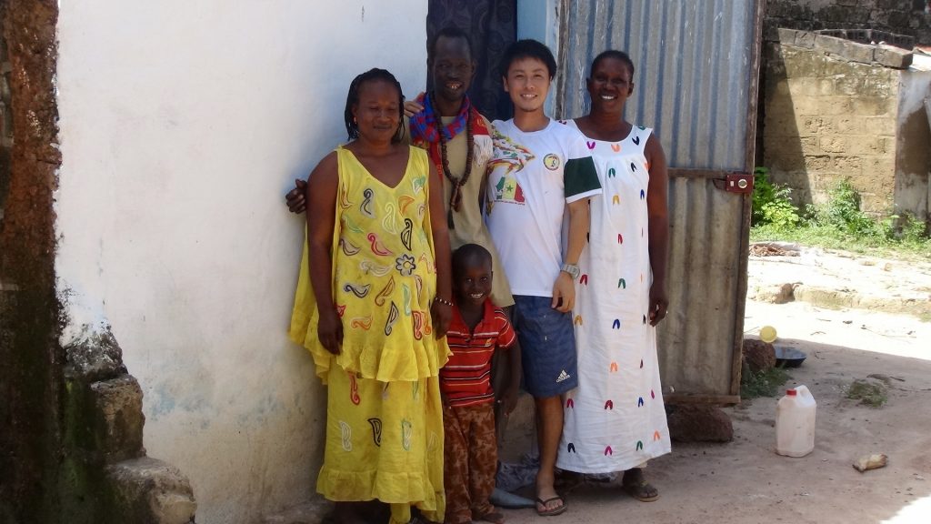 セネガルの民家の脇で松尾さんが大人3人、子ども1人と一緒に笑顔で立っている画像。