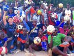 松尾さんが十数人のセネガル人と一緒にサッカーボールを持って笑顔で記念撮影している画像