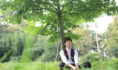 北原しんのすけさんが木の下で白杖を横に立てかけて座っている画像