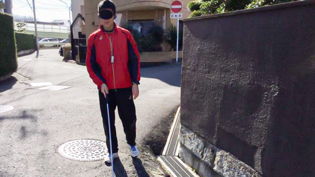 歩行訓練の実習中の高橋さん。アイマスクをして白杖を使っている。