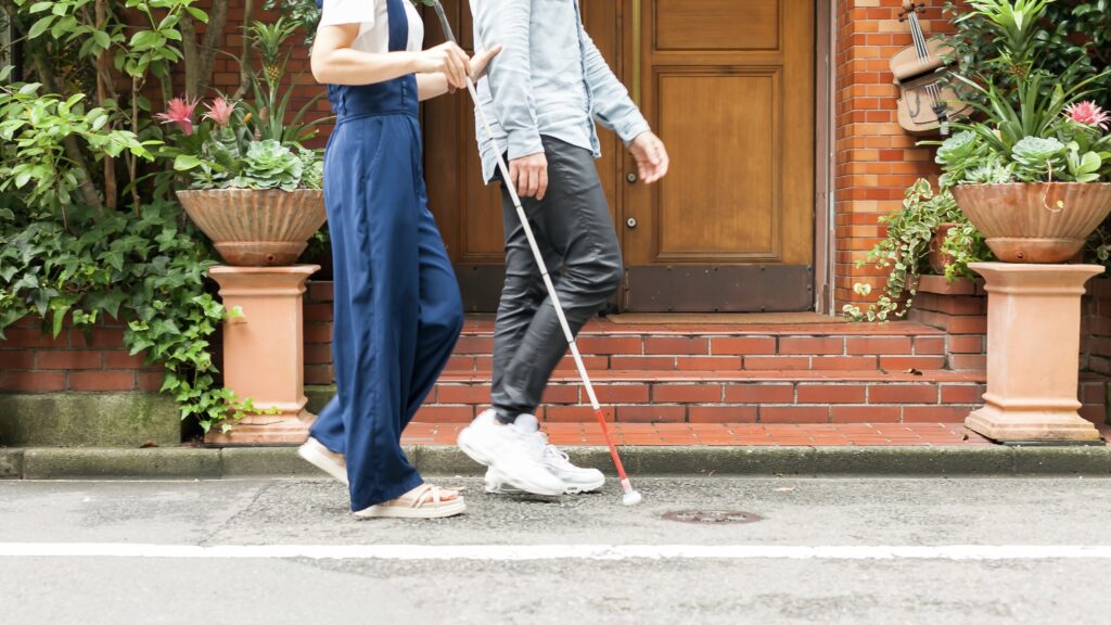 屋外を白杖で歩く女性と、同行援護の男性。