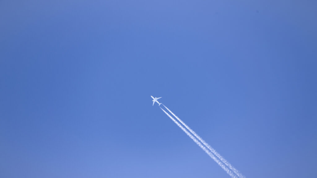 雲一つない青空に、遠くを飛んでいる飛行機と飛行機雲が見える。