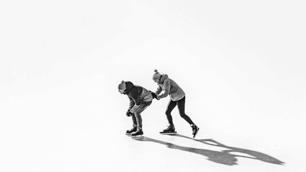 日の当たる場所で、アイススケートをする二人組の写真。一人が後ろからもう一人を支えている。