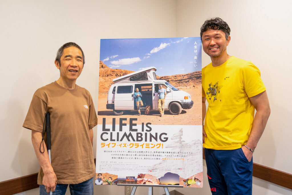 映画のポスターを挟んで、両側に小林さんと直也さんが立っている写真。