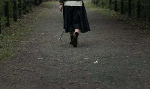 白状をもって、薄暗い中を一人で歩く女性の後ろ姿の写真。