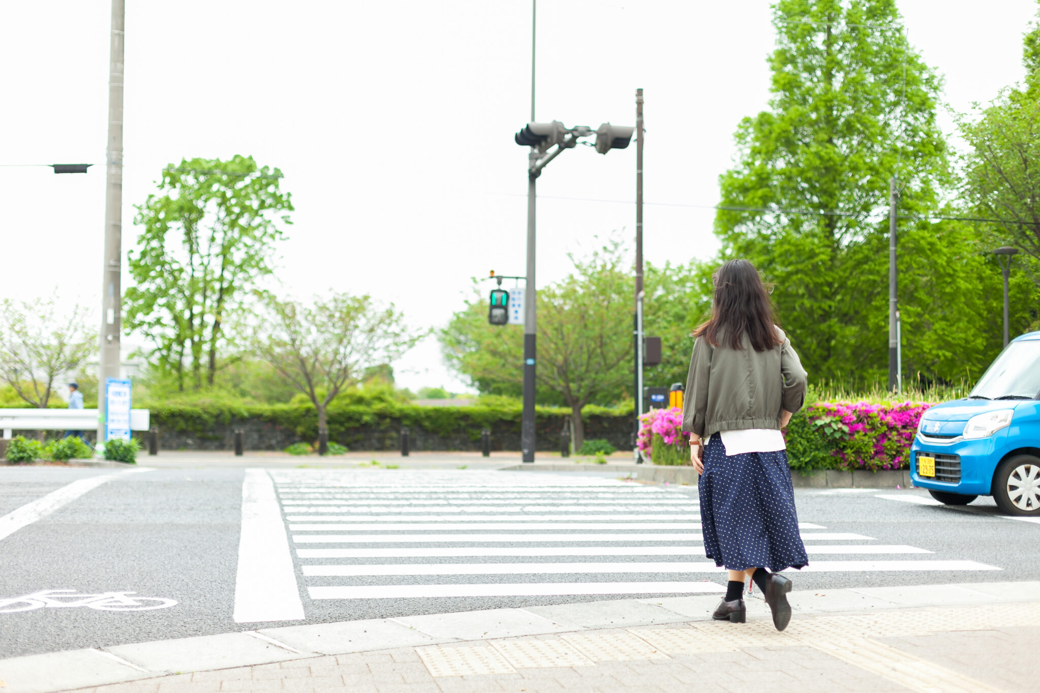 白杖を持った女性が青に変わった信号の横断歩道を渡ろうとしているところ。