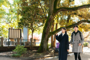 弱視の男性とガイドヘルパーが公園を歩いている写真。