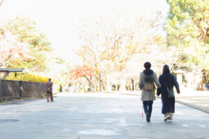 石畳の上を歩く、白杖を持つ男性とガイドヘルパーの女性