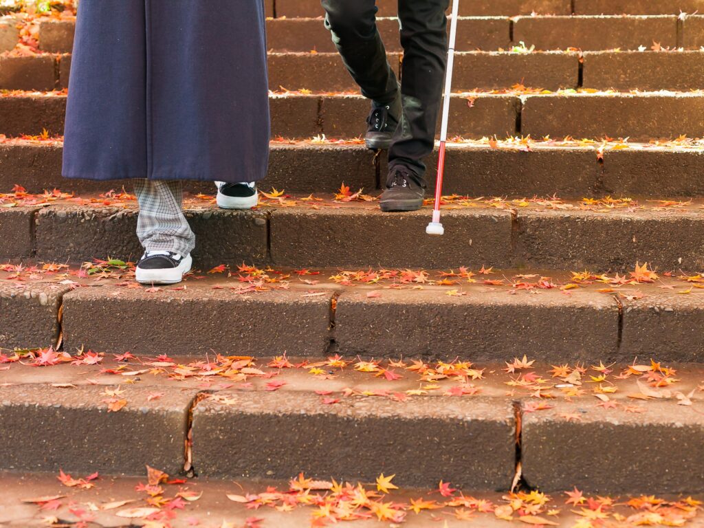 白杖の男性と晴眼者の女性が階段を下りている写真。
