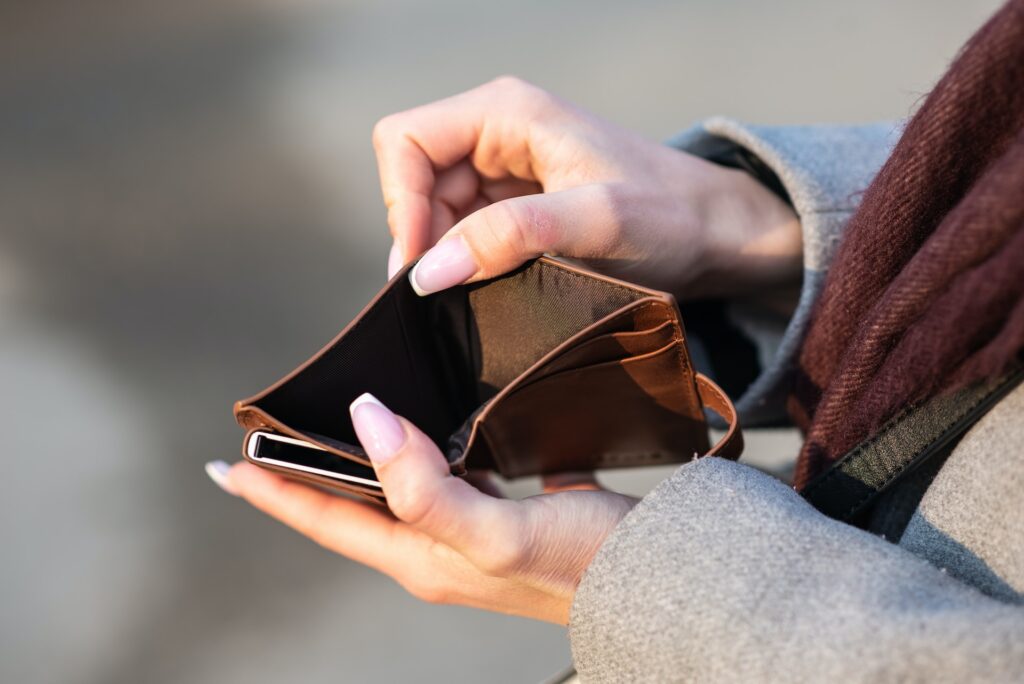 中身が空っぽの財布。マフラーを着用した人が両手で財布を広げている。