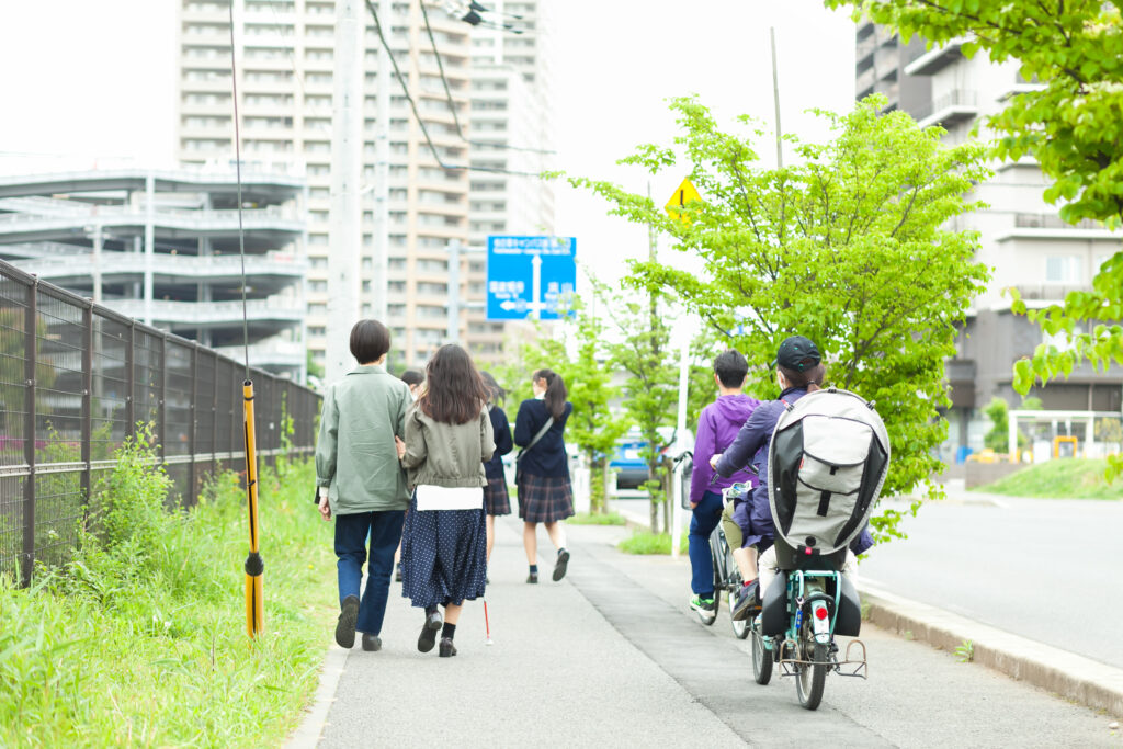 白杖の人とガイドヘルパーが歩いているそばを、自転車や人が追い抜いている写真。