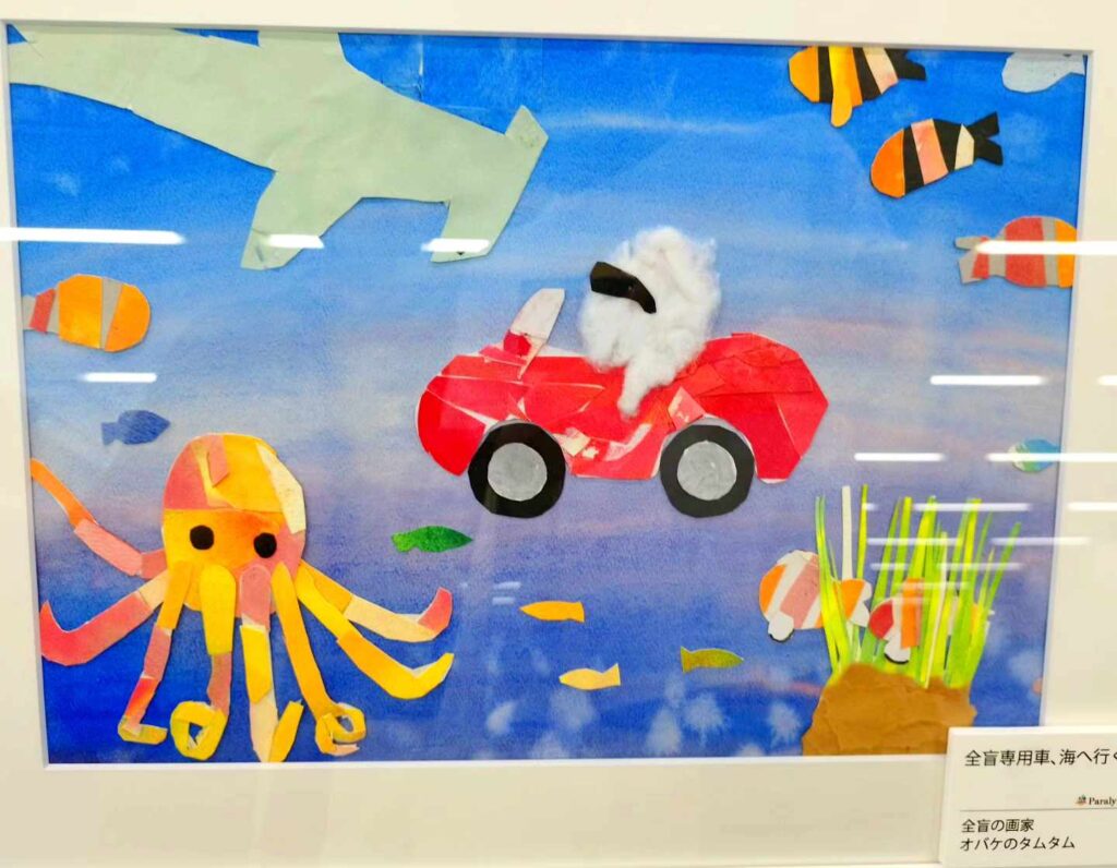 貼り絵作品の写真。海の中を車に乗ったオバケのタムタムが進んでいる。たこや魚、海藻などが見える。